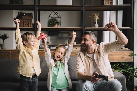Happy family celebrating triumph while playing video game with joysticks at home.の写真素材