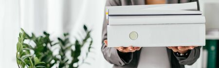 panoramic shot of woman holding folders while standing near flowerpot with plantsの写真素材