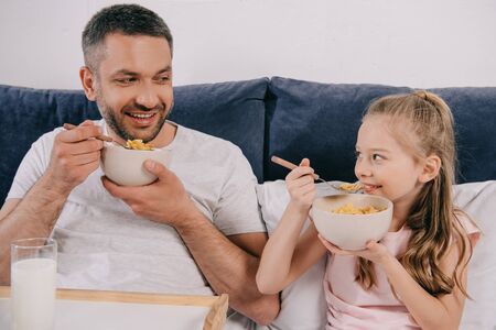 cheerful dad with adorable daughter having breakfast in bed on fathers day togetherの写真素材