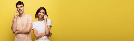 panoramic shot of young man and woman talking on smartphones on yellow backgroundの写真素材