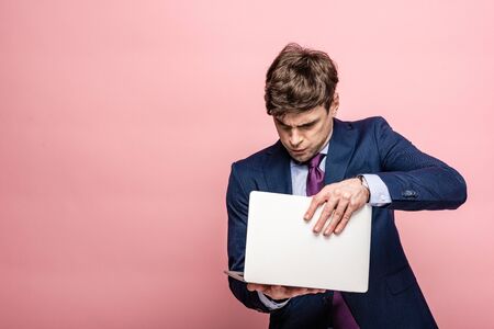 serious businessman in suit opening laptop on pink background