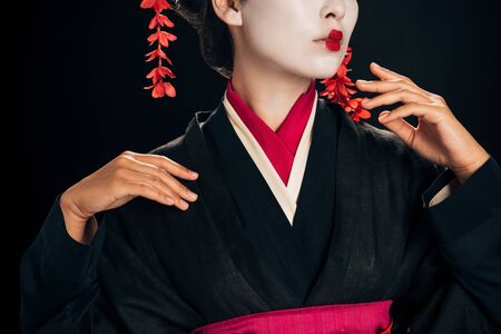 partial view of beautiful geisha in black and red kimono gesturing isolated on blackの写真素材