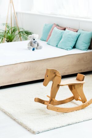 selective focus of wooden rocking horse near bed with white bedding, pillows and teddy bearの写真素材