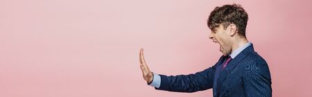 panoramic shot of angry businessman showing stop gesture isolated on pinkの写真素材