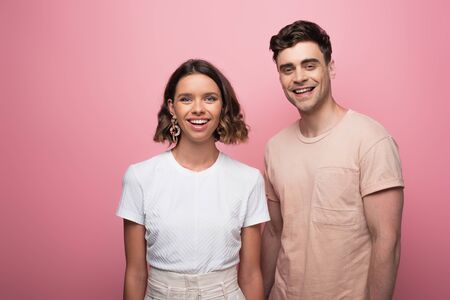 young, cheerful man and woman looking at camera on pink background