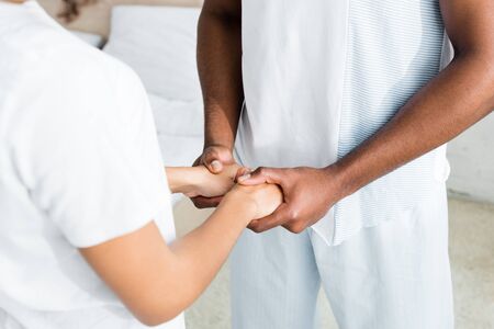 cropped view of african american man holding hands with woman in white clothes