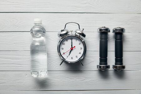 flat lay with silver alarm clock, bottle of water and dumbbells on wooden white backgroundの写真素材
