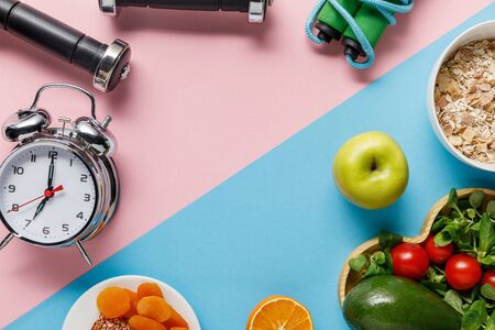 top view of delicious diet food and sport equipment with alarm clock on blue and pink backgroundの写真素材