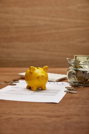 selective focus of bankruptcy form, coins, yellow piggy bank, calculator and glass jar with dollar banknotes on wooden tableの写真素材