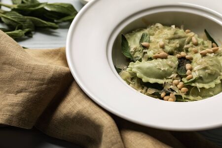 close up view of green ravioli served in white plate with sage, pine nuts and grated cheese near sackclothの写真素材