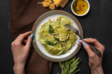 top view of woman eating delicious green ravioli with sage and pine nuts at black wooden tableの写真素材
