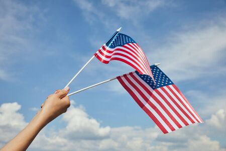 Cropped view of  woman holding american flags in hand on blue sky background
