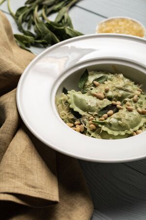 close up view of green ravioli served in white plate with sage, pine nuts and grated cheese near napkinの写真素材