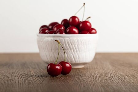 selective focus of red cherries in bowl on wooden table isolated on whiteの写真素材