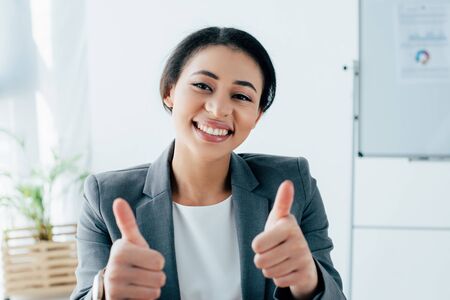 cheerful latin businesswoman showing thumbs up while smiling at cameraの写真素材