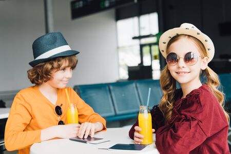 preteen kids sitting at table with orange juice in departure loungeの写真素材