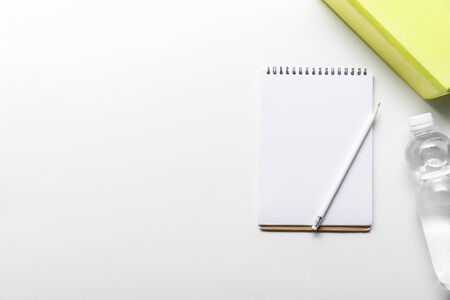 top view of water in bottle and blank notebook with pencil near box on white background