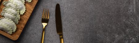 served on wooden board green ravioli near cutlery on grey background with copy space, panoramic shot