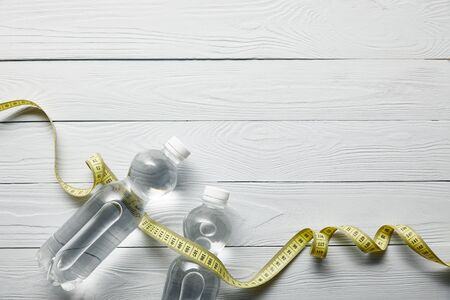 top view of bottles with water and yellow measuring tape on wooden white background with copy spaceの写真素材