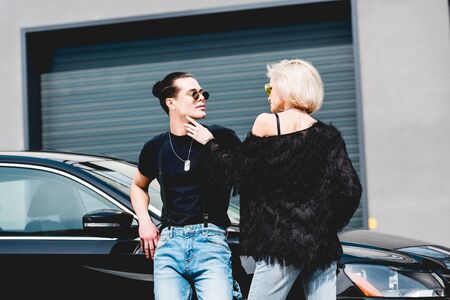beautiful stylish couple posing near black car and garage
