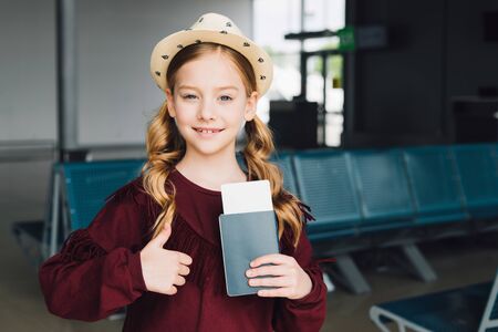 cute preteen kid with passport and air ticket showing thumb up in airport