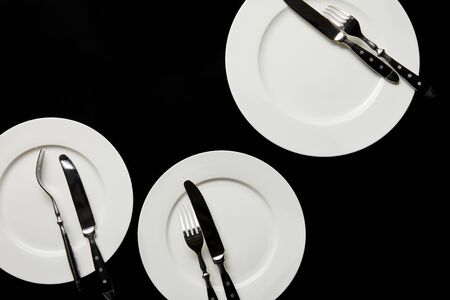 top view of white round plates with cutlery isolated on blackの写真素材