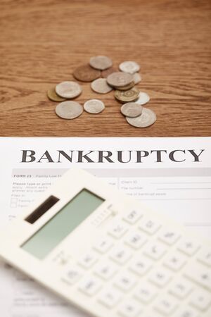 selective focus of bankruptcy form, calculator and coins on brown wooden tableの写真素材