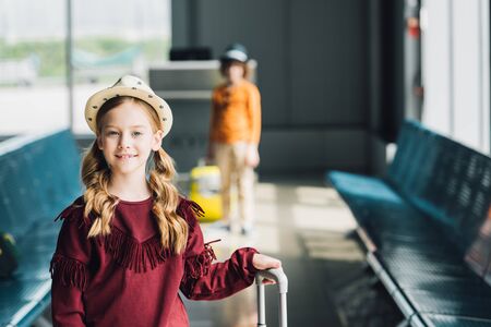 selective focus of cute preteen kid in waiting hall in airport with suitcaseの写真素材