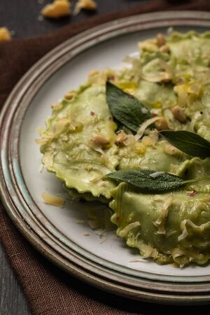 close up view of green ravioli with melted cheese, pine nuts and green sage leaves in retro plateの写真素材
