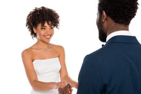 selective focus of happy african american bride looking at bridegroom while holding hands isolated on whiteの写真素材