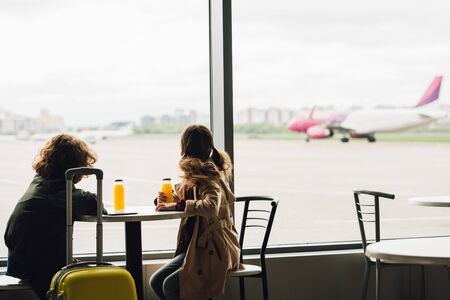two kids sitting in waiting hall and looking out window on planeの写真素材