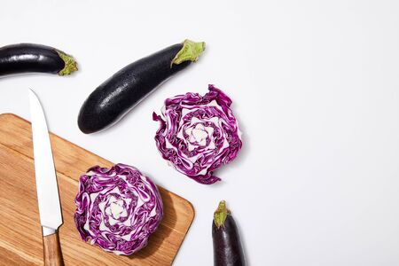 top view of red cabbage and eggplants on wooden chopping board and knife on white backgroundの写真素材