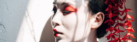 portrait of beautiful geisha with red and white makeup in sunlight with shadows, panoramic shotの写真素材