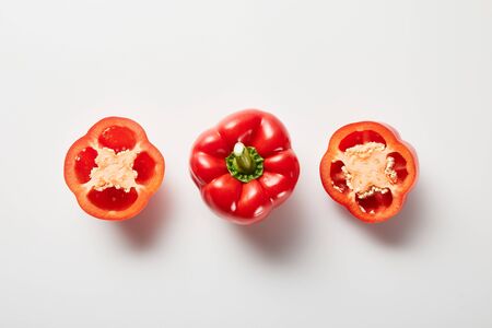 top view of red organic cut and whole bell peppers on white background