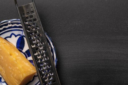 top view of sharp grater with cheese on ornate plate on black backgroundの写真素材