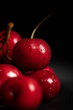 close up view of red tasty and ripe cherries with water drops on black backgroundの写真素材
