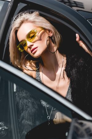 beautiful fashionable sexy young woman in glasses posing in car with eyes closed