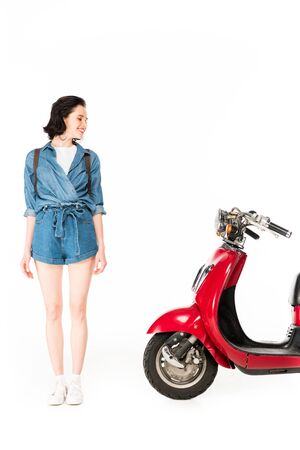 full length view of girl looking at red scooter isolated on whiteの写真素材