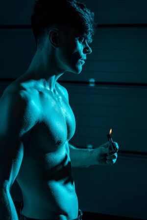 sexy shirtless muscular man holding lighter in darkness