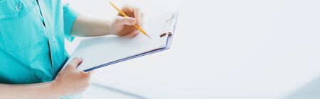 panoramic shot of doctor in blue uniform writing on clipboardの写真素材