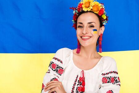 happy brunette young woman in national Ukrainian costume and floral wreath with flag of Ukraine on backgroundの写真素材