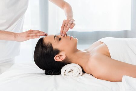 cropped view of masseur touching nose of attractive brunette woman lying on massage tableの写真素材