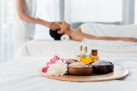 selective focus of tray with bottles of oil, bowls with sea salt and flowers near women in spa centerの写真素材