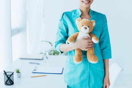 partial view of young latin doctor holding teddy bear while standing near workplaceの写真素材