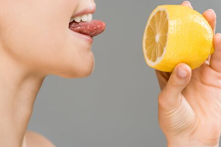 cropped view of cheerful girl holding half of lemon isolated on greyの写真素材