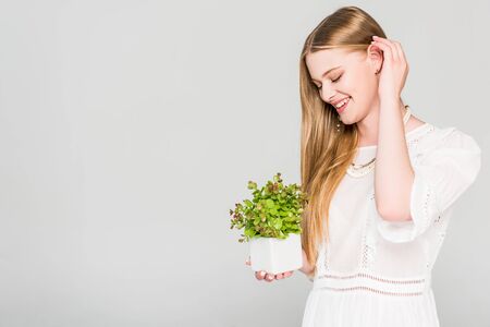 happy girl holding flowerpot with plant isolated on greyの写真素材