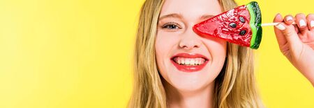 panoramic shot of beautiful smiling girl with lollipop in shape of watermelon Isolated On yellowの写真素材