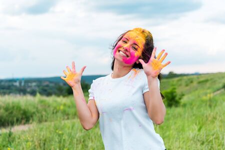 happy woman with pink and yellow holi paint on face and handsの写真素材