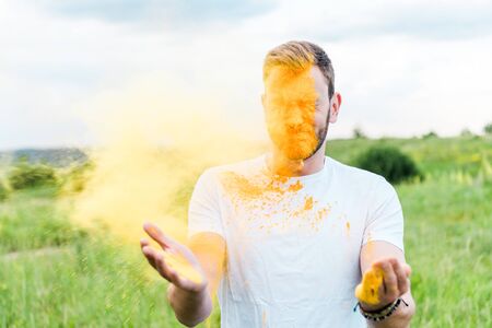 young man with closed eyes near splash of yellow holi paintの写真素材