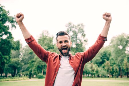 excited young man standing in park and putting hands in airの写真素材